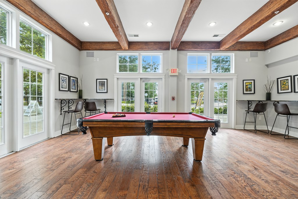 A pool table is in the middle of a room with wood floors and a high ceiling.