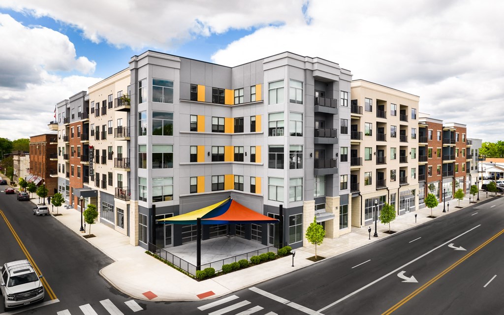 Madamore Apartments exterior with a sidewalk, trees, and a road with cars.
