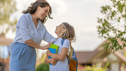 A woman in a blue dress is giving a hug to a young girl in a white shirt and blue jeans.