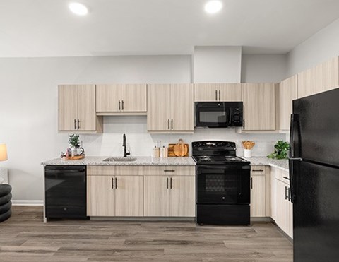 A black fridge sits in a kitchen with wooden cabinets and a black oven.