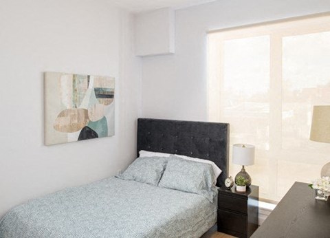 A bedroom with a bed, nightstand, and a painting on the wall.