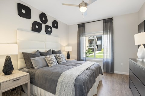 A bedroom with a large bed, a ceiling fan, and a window with curtains.