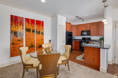 A dining room with a table set for two and a painting of a forest scene on the wall.