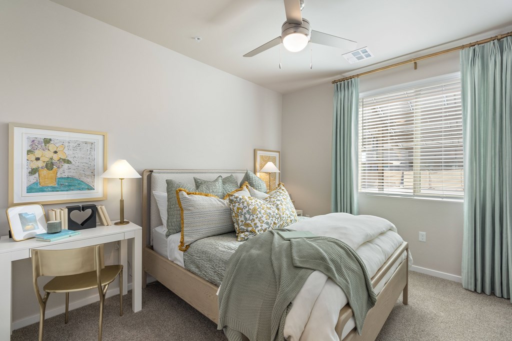 A bedroom with a bed, desk, chair, and window.