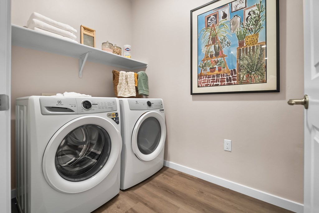 A laundry room with two front loading washing machines and a painting on the wall.
