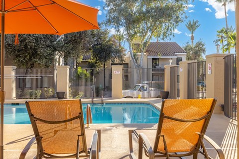 Two chairs and an umbrella are on a patio next to a pool.