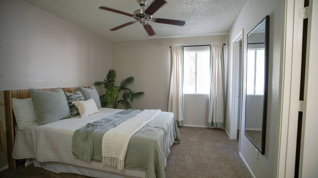 A bedroom with a bed, pillows, a ceiling fan, and a window with curtains.