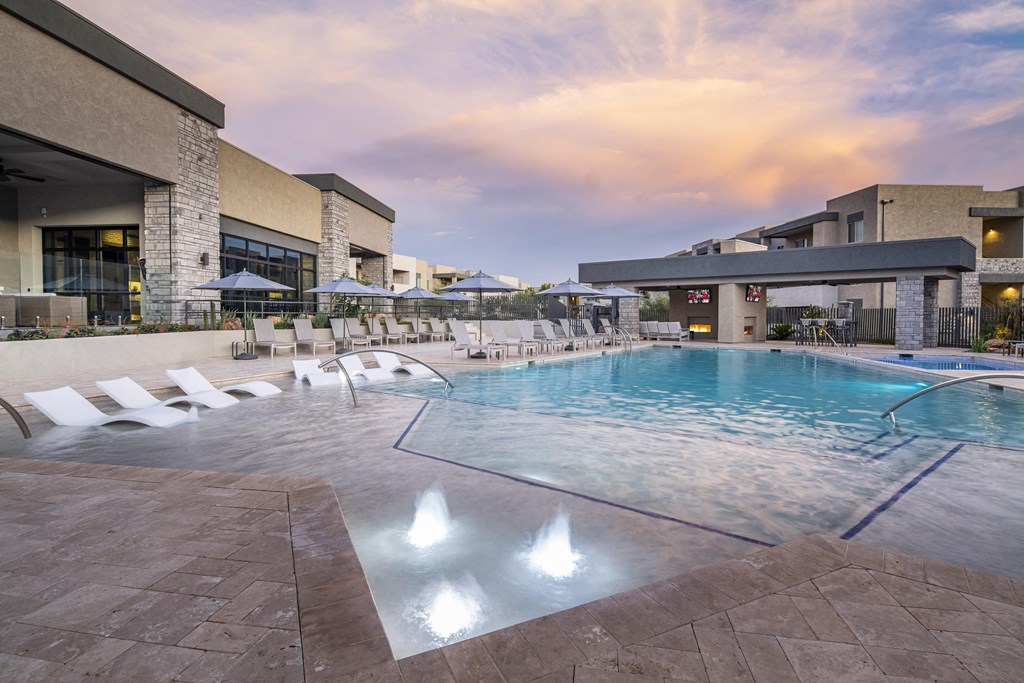 a swimming pool with chaise lounge chairs and umbrellas in front of a hotel