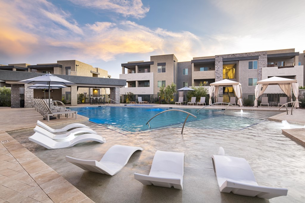 a swimming pool with lounge chairs and umbrellas in front of a building