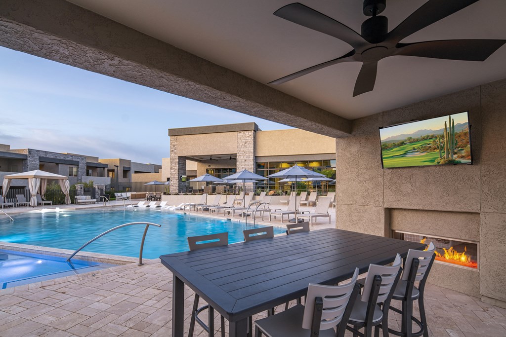 a patio with a table and chairs and a pool in the background
