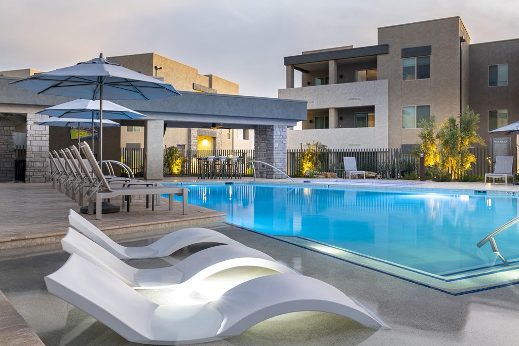 a swimming pool with lounge chairs and umbrellas in front of a building