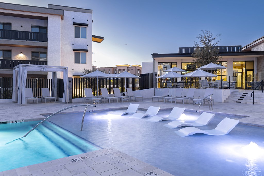 a swimming pool with chairs and umbrellas at night
