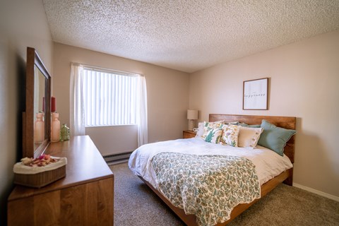 A bedroom with a bed, nightstand, and a window with blinds.