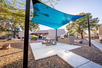 A blue shade sail over a picnic table in a sunny outdoor area.