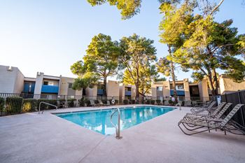 A swimming pool surrounded by trees and chairs in front of a building.