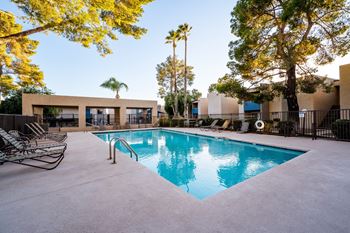 A pool surrounded by trees and chairs.