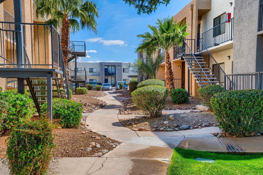 a pathway between two apartment buildings with palm trees
