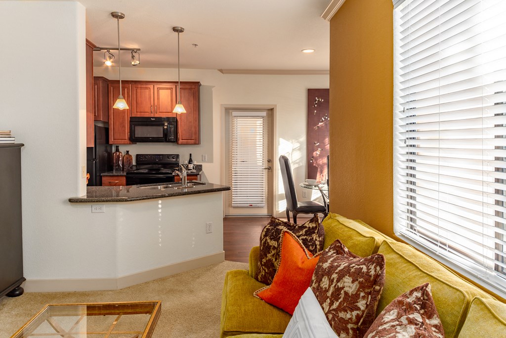 a living room with a yellow couch and a kitchen in the background