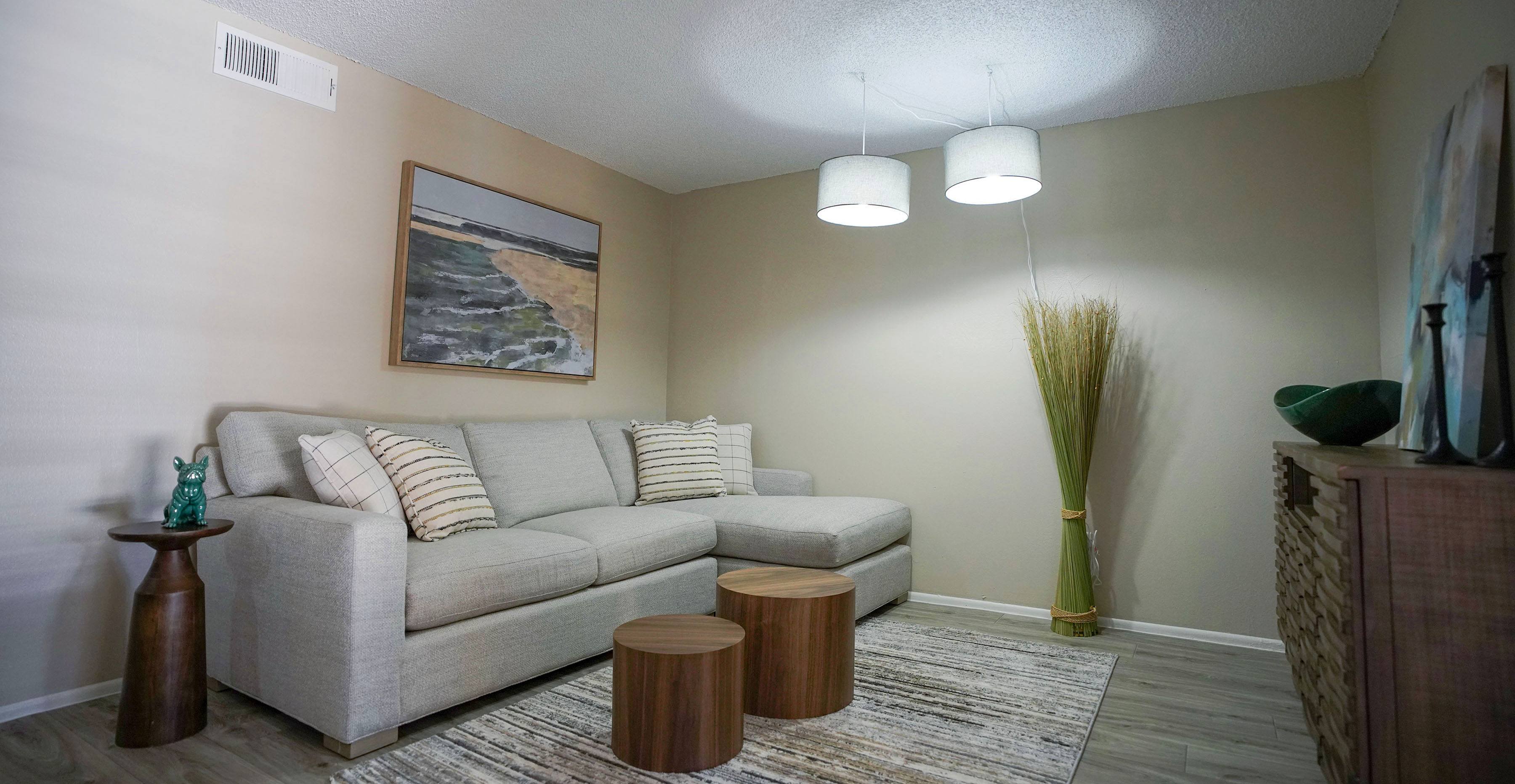 A living room with a grey couch, a painting of a beach scene, and a tall green plant.