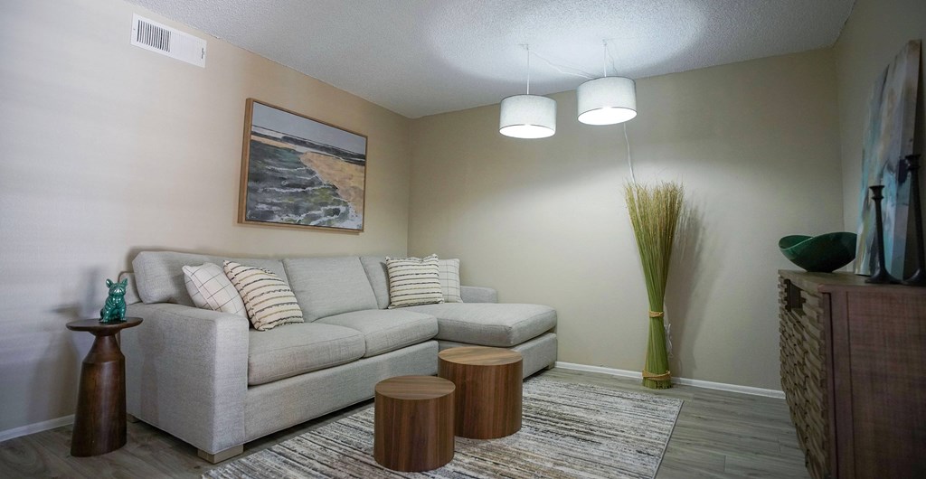 A living room with a grey couch, a painting of a beach scene, and a tall green plant.