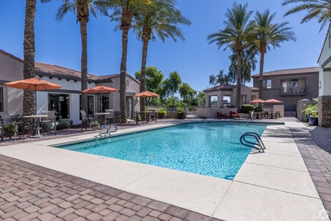 A swimming pool surrounded by palm trees and patio furniture.