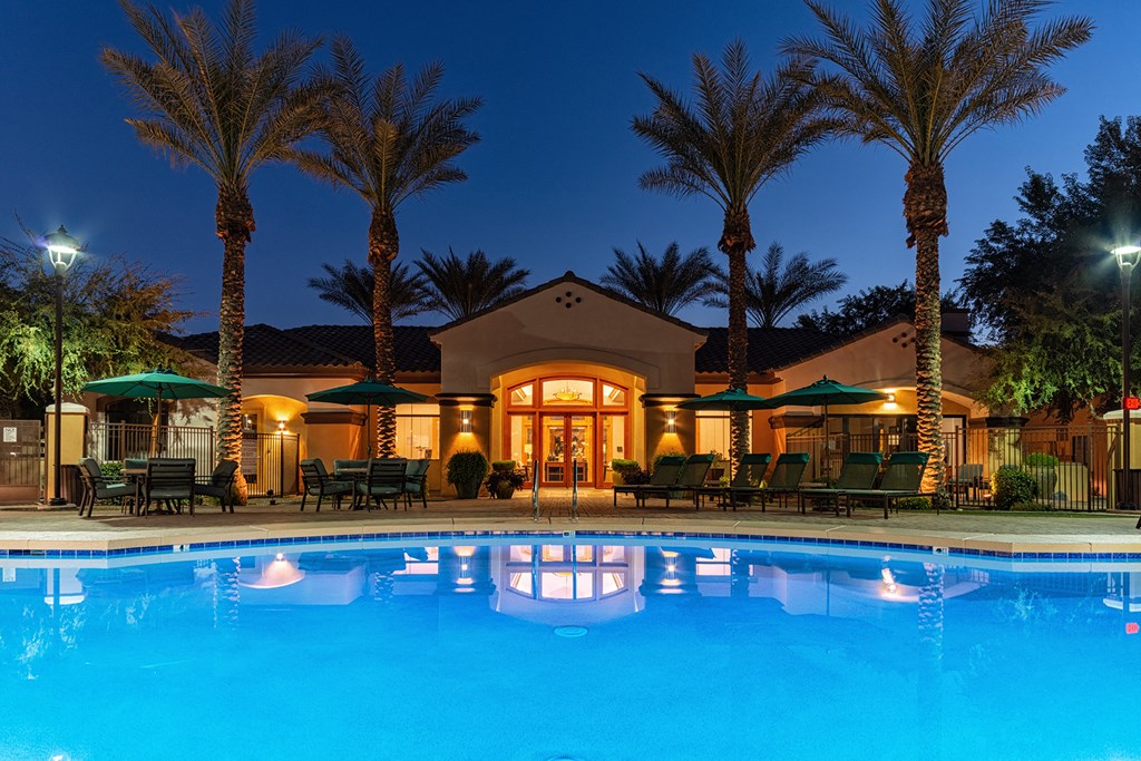 a resort style swimming pool with lounge chairs and umbrellas at night