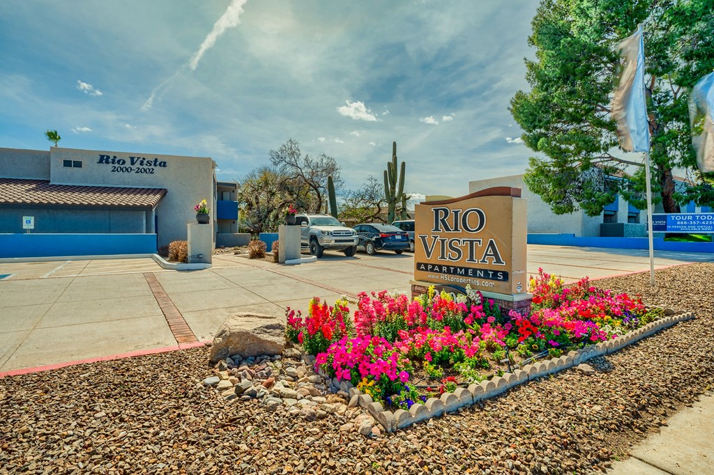 a sign for the rio vista entrance with flowers in front of a building