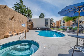 A swimming pool with a blue umbrella and a hot tub in the foreground.