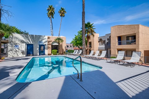 our resort style swimming pool is next to a building and palm trees