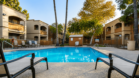 A pool surrounded by a fence and chairs with a building in the background.