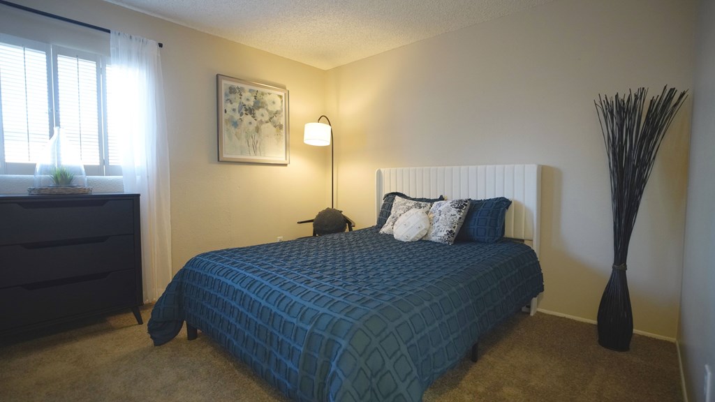 A bedroom with a blue bedspread and a black floor lamp.