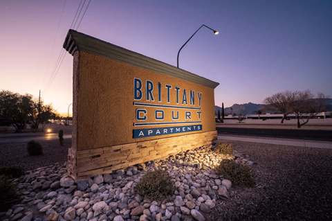 A wooden sign that says Brittany Court Apartments is in front of a street lamp.