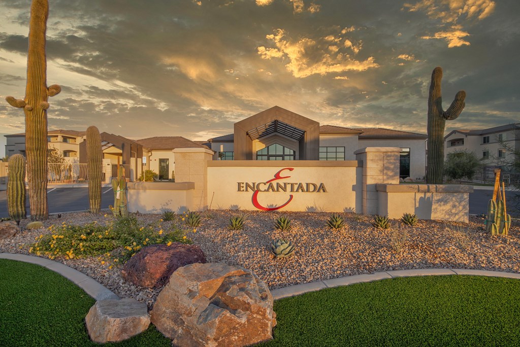 The image shows a building with the word "Encantada" on it, surrounded by cacti and rocks.