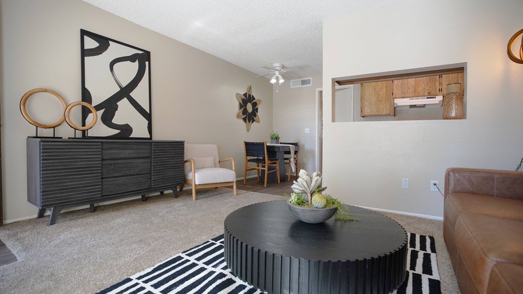 A living room with a black and white rug, a round coffee table with a vase of flowers, a brown leather couch, and a wooden cabinet with a decorative piece on top.