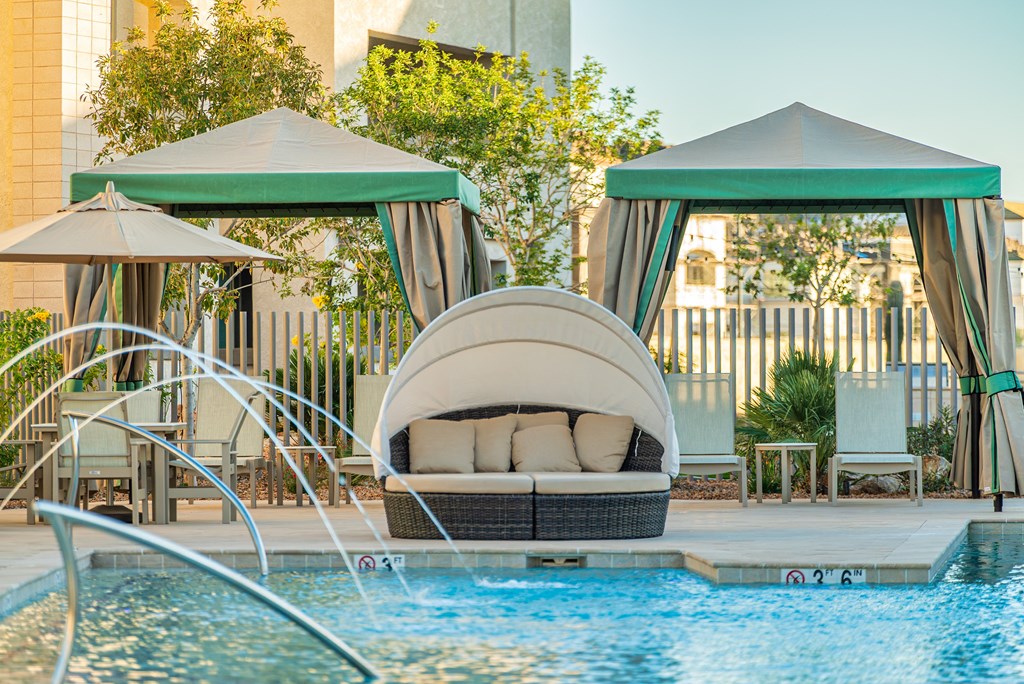 A poolside lounge area with a white couch and green umbrellas.