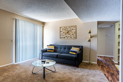 A living room with a black couch and a glass coffee table.