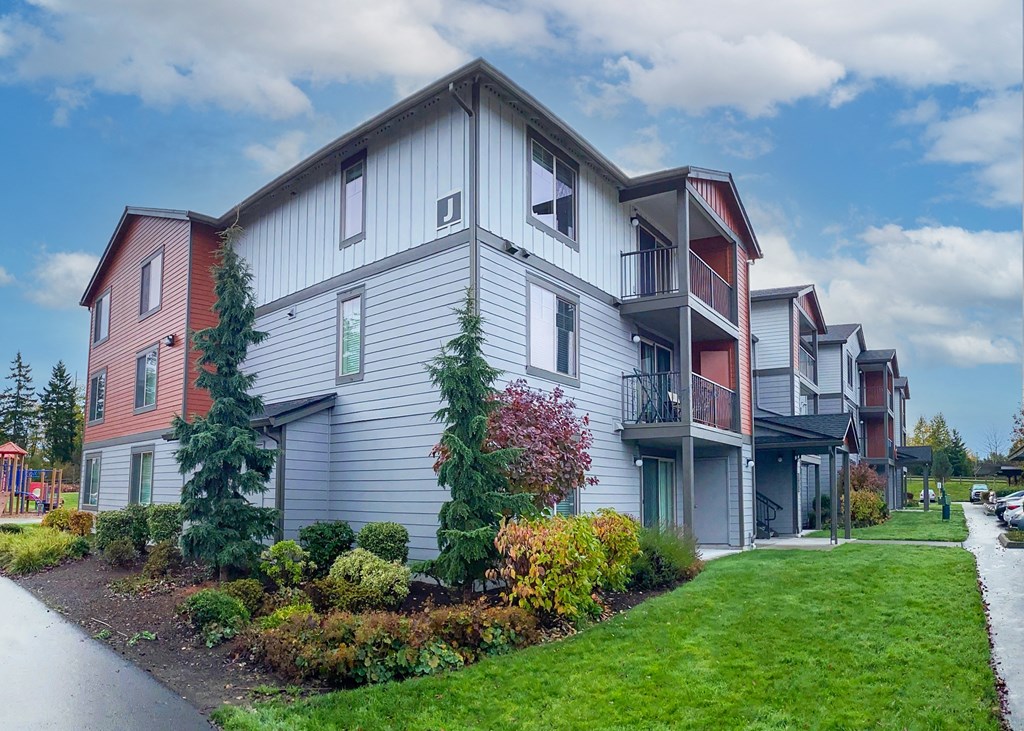 a white and red apartment building with balconies and a green yard