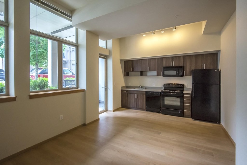 an empty living room with a kitchen and a large window