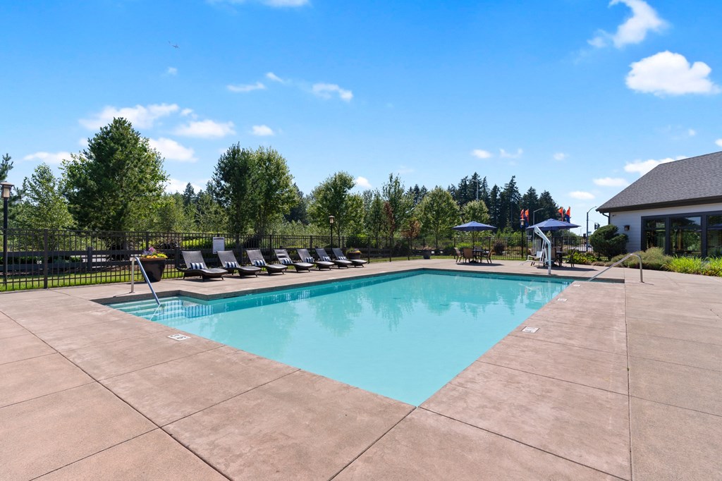 a swimming pool with lounge chairs around it in front of a house
