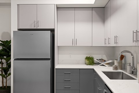 A modern kitchen with a grey refrigerator and white countertops.