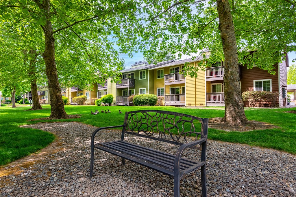 a park bench on a gravel path in front of a yellow apartment building