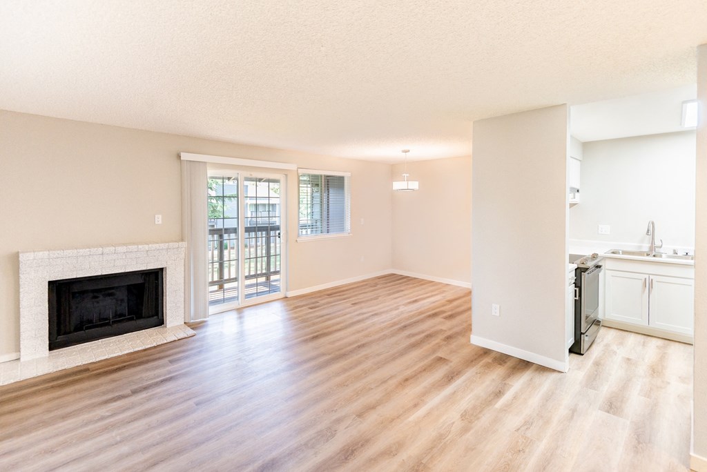 an empty living room with a fireplace and a kitchen