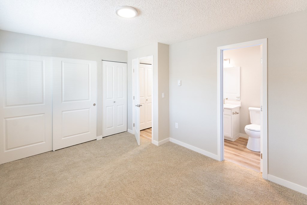 an empty bedroom with white doors and a bathroom