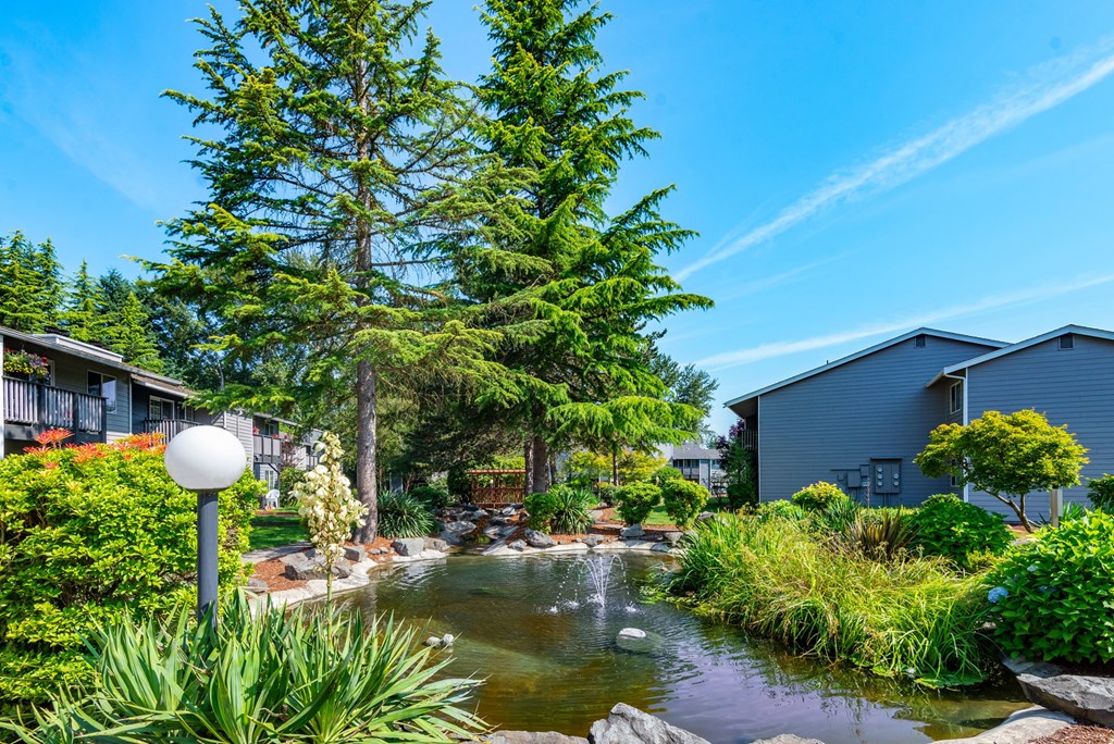 a garden with a pond and trees in front of houses