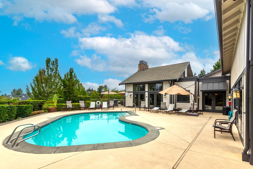 a swimming pool with lounge chairs and umbrellas in front of a house