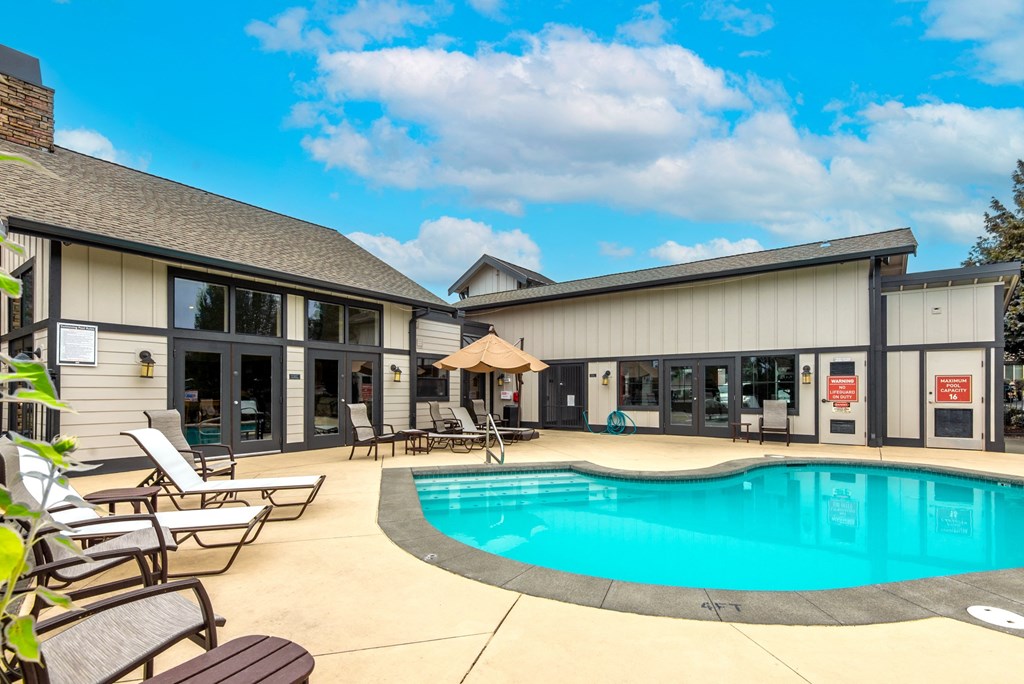 a swimming pool with chaise lounge chairs and umbrellas in front of a building