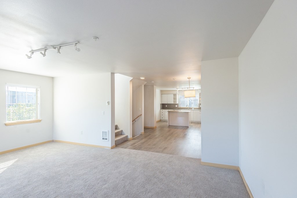 an empty living room with a kitchen in the background
