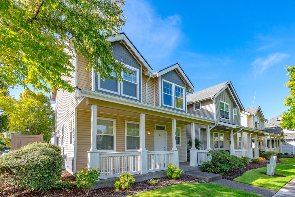a yellow house with a porch and a tree in front of it