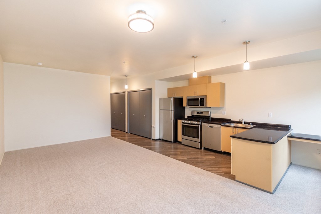 an empty living room with a kitchen with stainless steel appliances