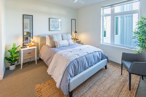 A bedroom with a large bed, a chair, and a potted plant.